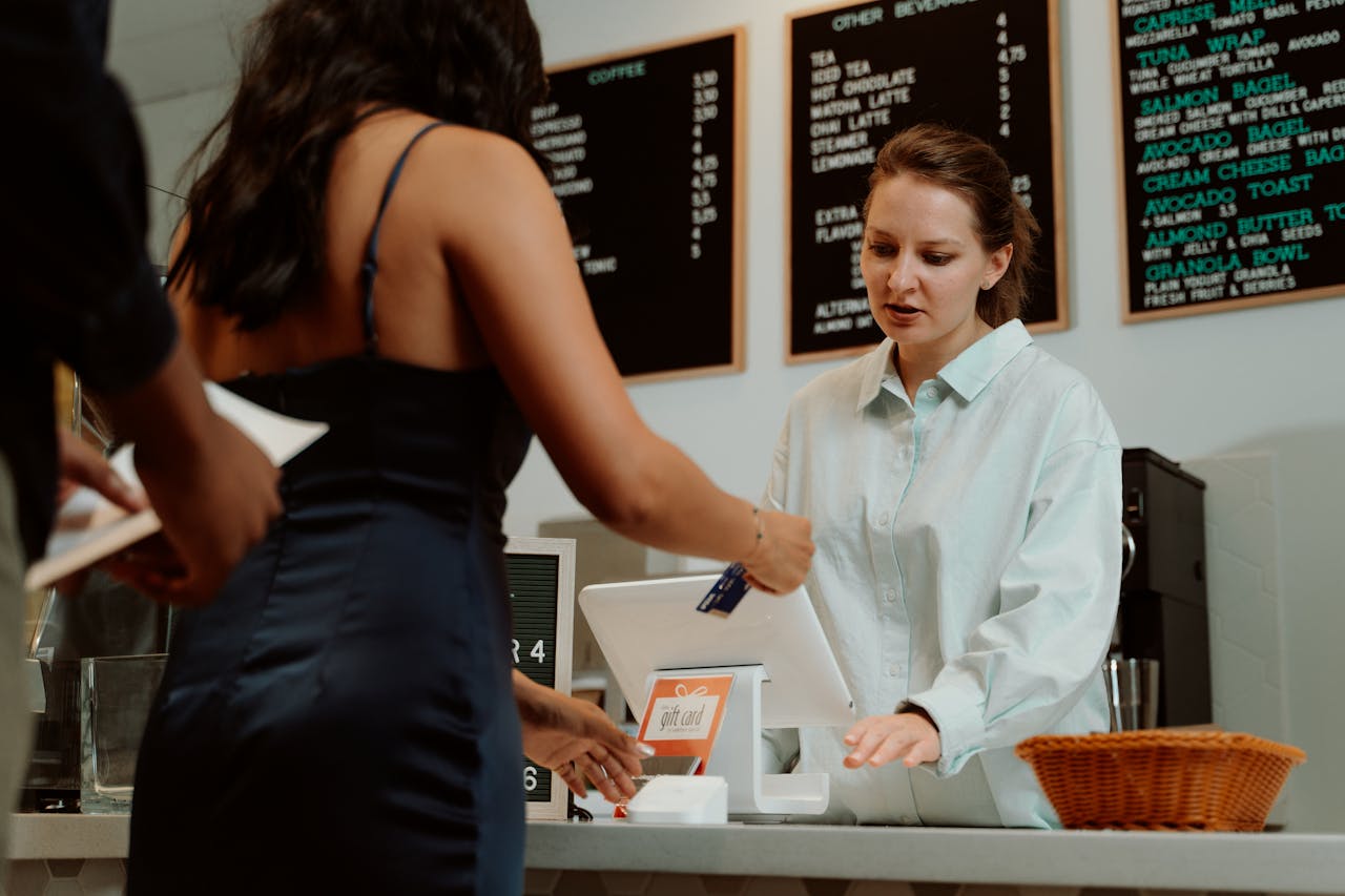 A customer pays with a card at a coffee shop as a barista assists.