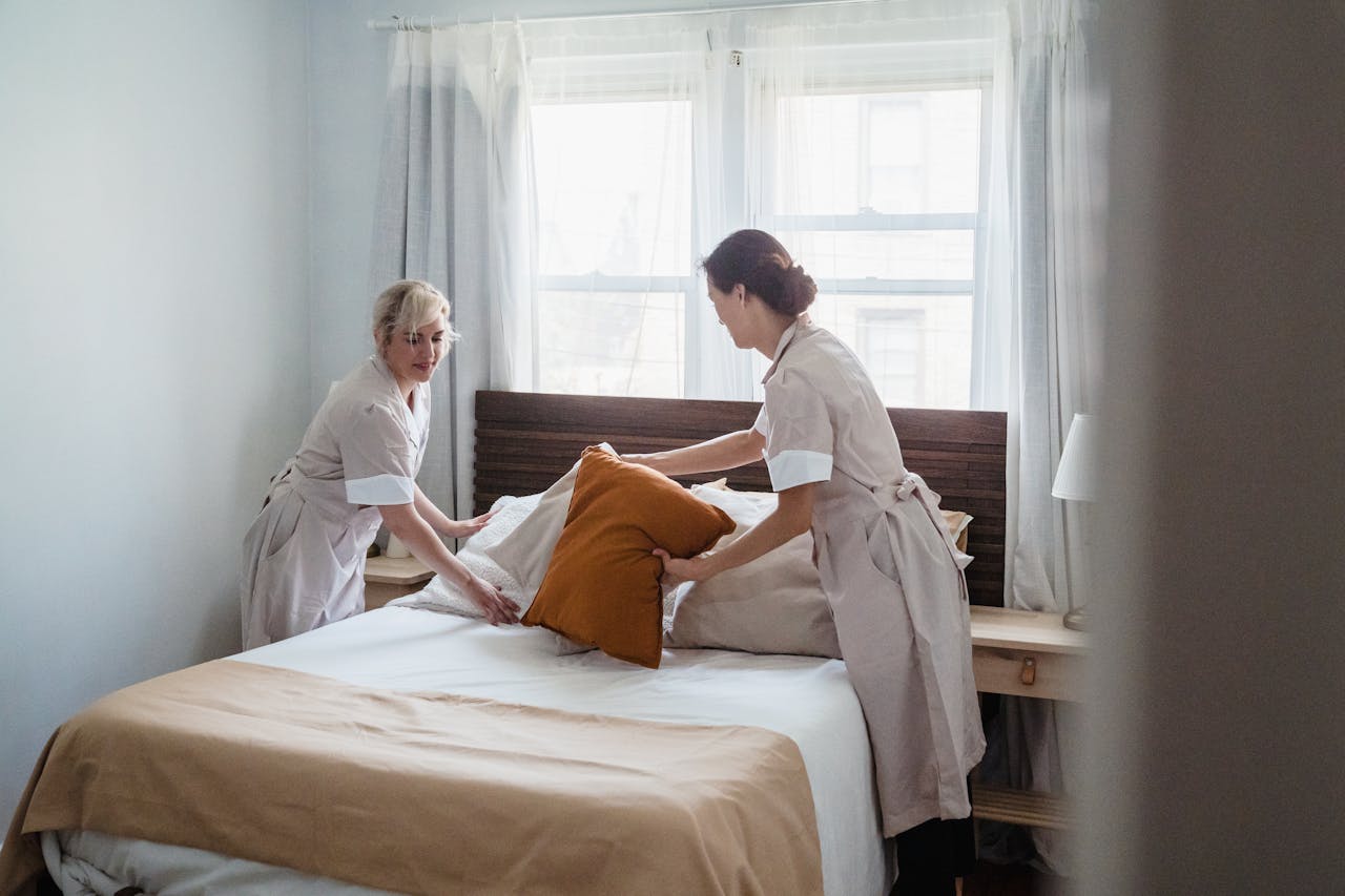 Two housekeepers organizing bed linen in a bright, cozy bedroom.